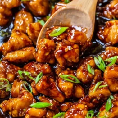 A plated dish of Honey Garlic Chicken garnished with sesame seeds and green onions.