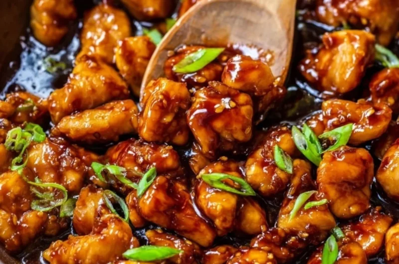 A plated dish of Honey Garlic Chicken garnished with sesame seeds and green onions.